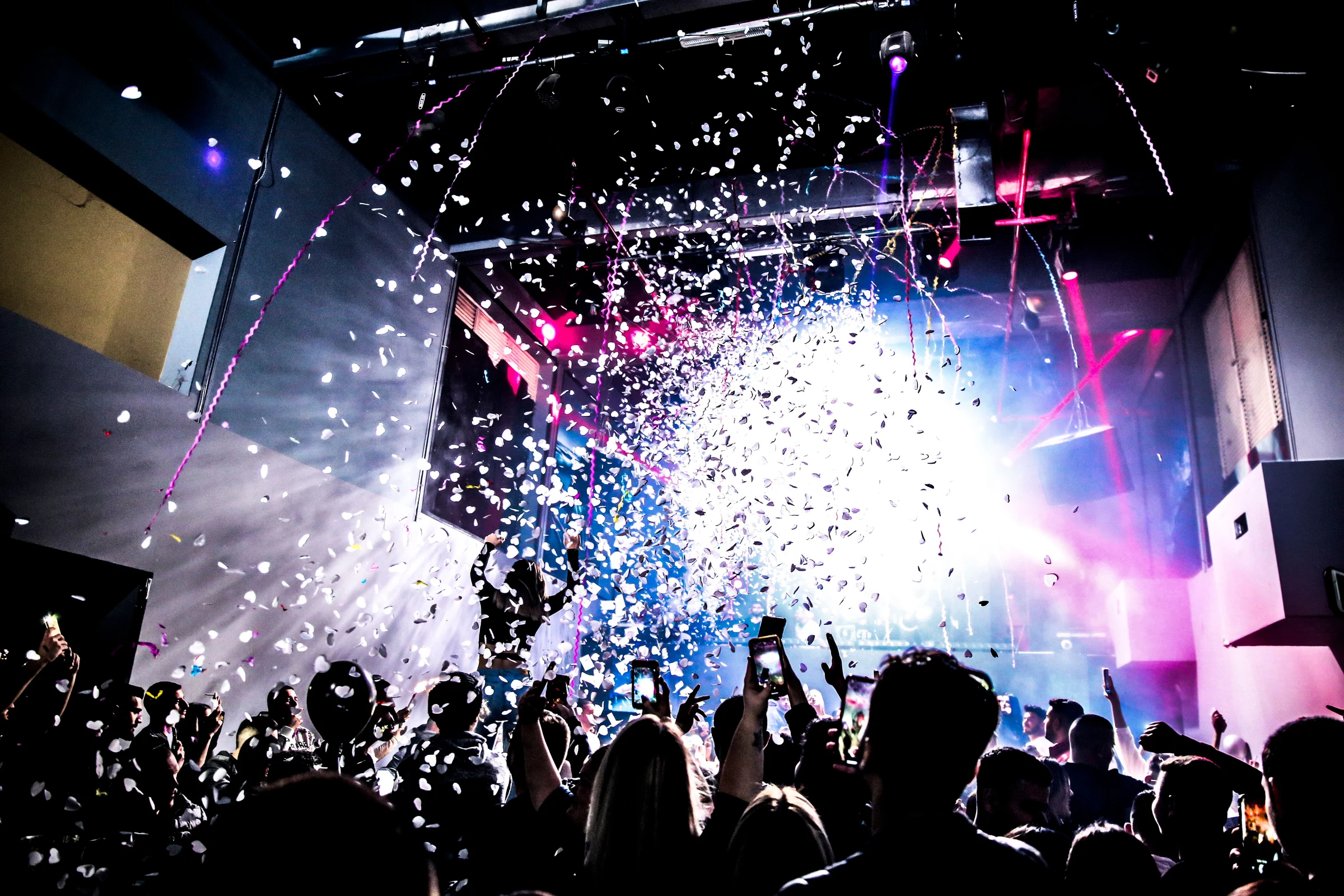 An energetic crowd celebrating with raised hands, a shower of confetti and vibrant event lighting