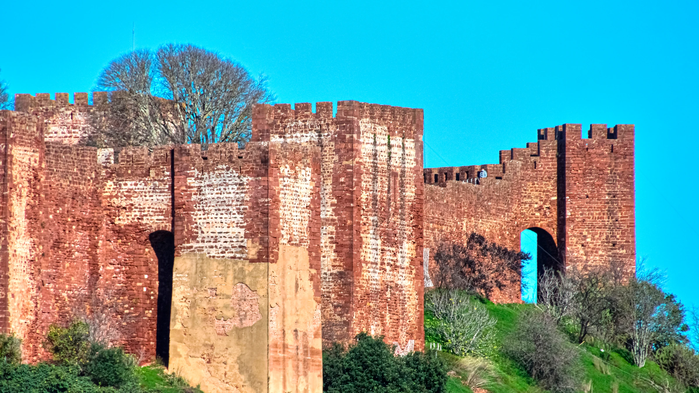 Imposing red sandstone walls and crenellated towers of Silves Castle beneath a clear blue sky