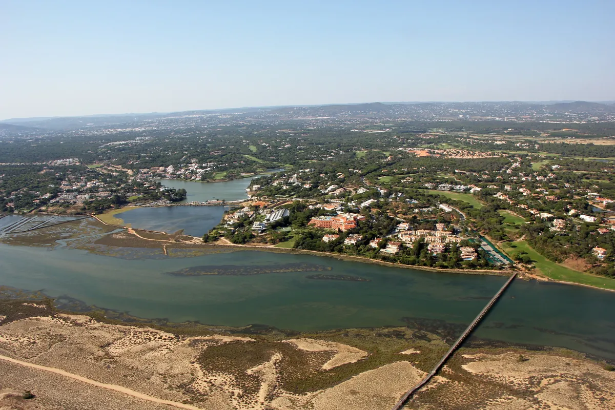 Aerial view over Quinta do Lago, its lagoon, coastal dunes and surrounding buildings.