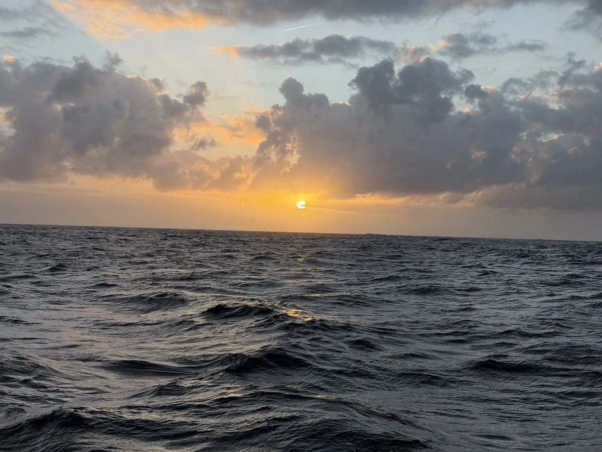 Sun setting over the Atlantic beneath scattered clouds.