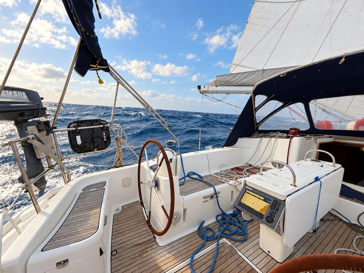 Wooden steering wheel and seating in ZERO’s cockpit beneath the rigging at sea.