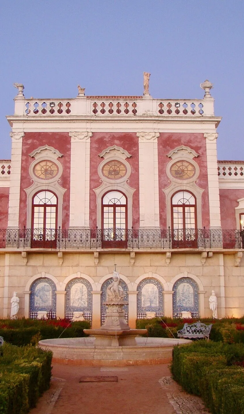 The pink-and-white façade of Palácio de Estoi with formal gardens in front.