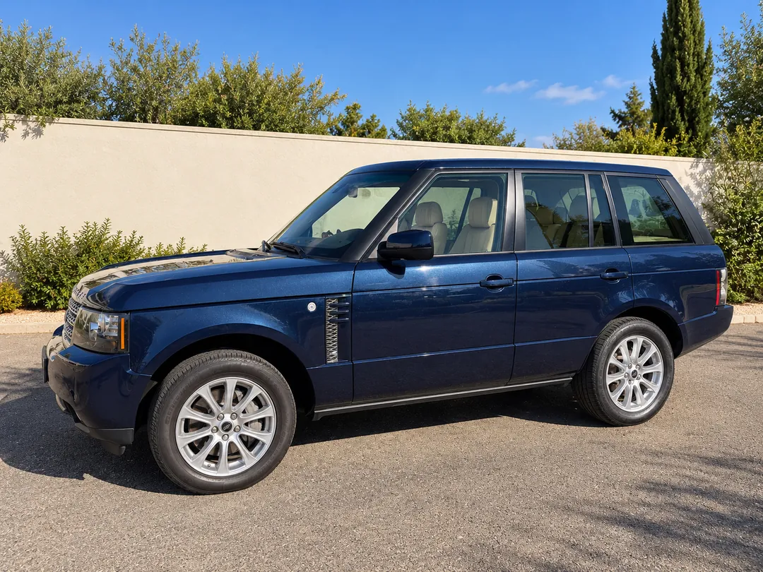 Side view of the navy Range Rover L322 beside a pale wall and trees.
