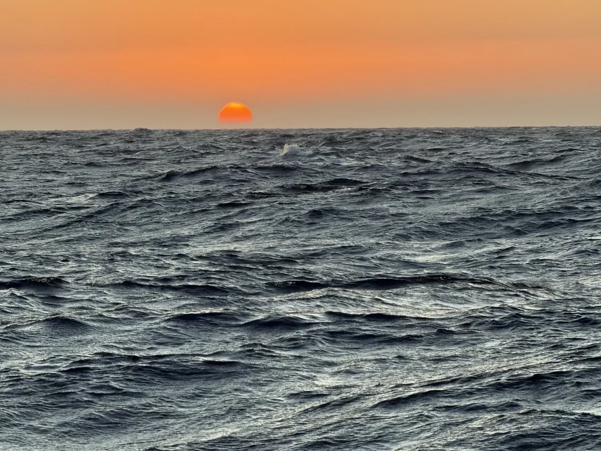 Orange sun at the horizon above the open sea.