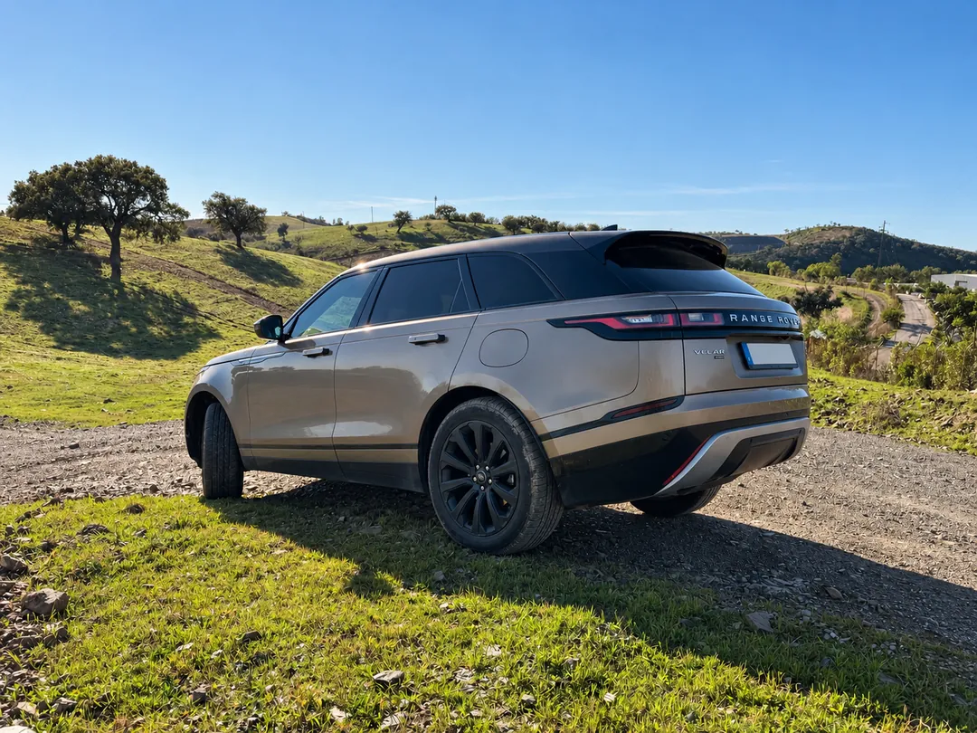 Rear three-quarter view of the Range Rover Velar on a country track among green hills.