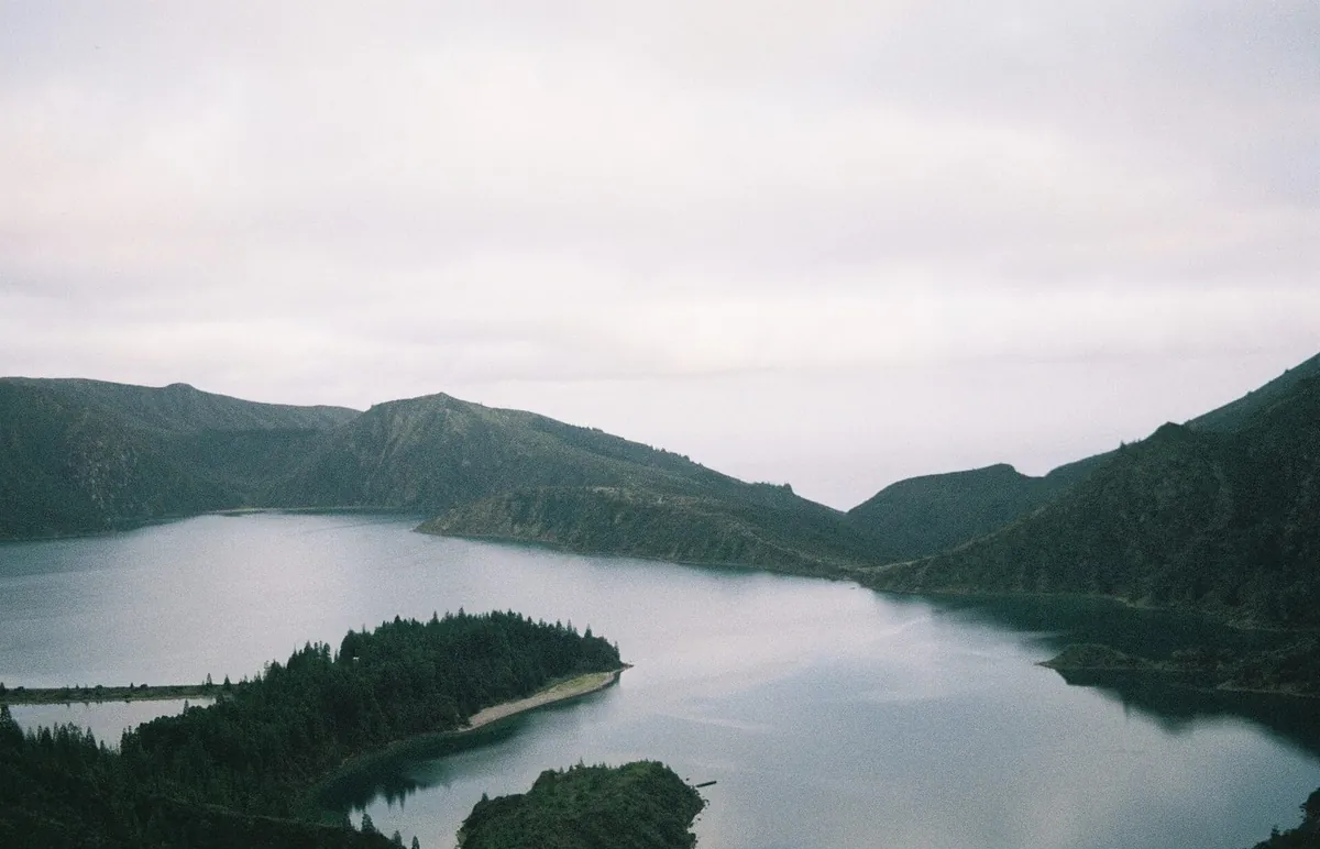 Lagoa do Fogo beneath cloud and mist, with wooded crater slopes around the water.