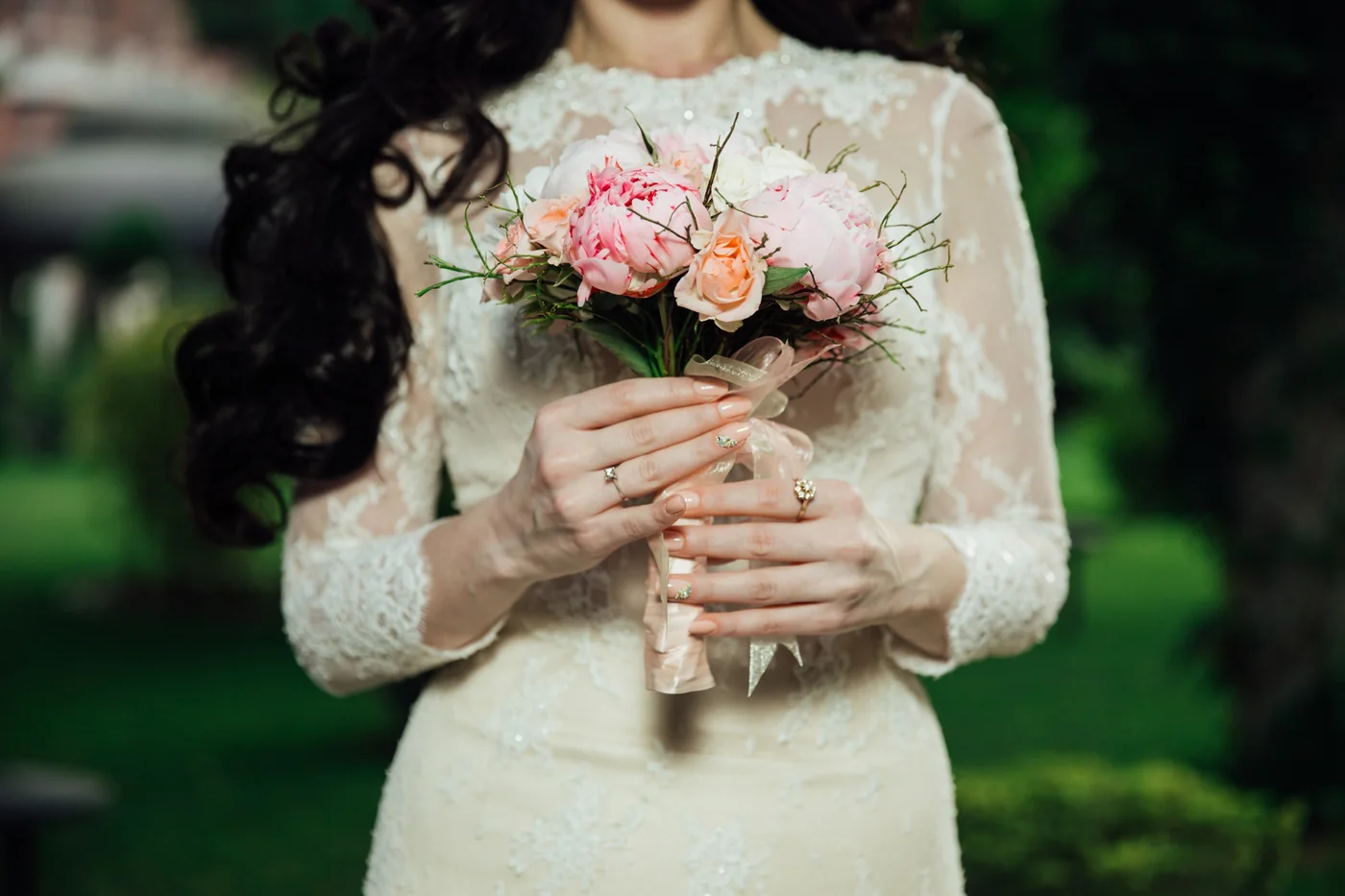 A person in a lace dress holding a bouquet of pink and peach flowers.