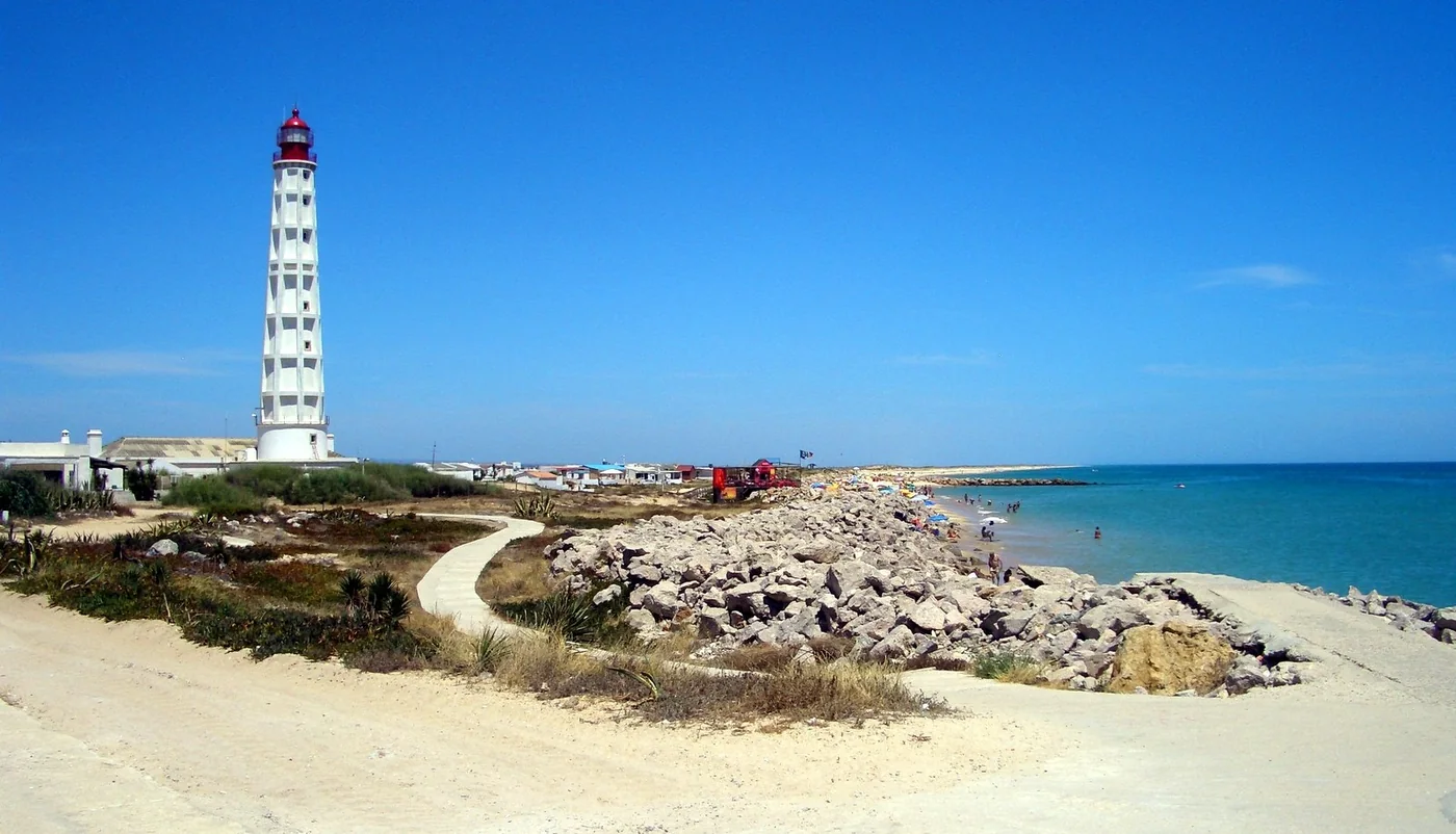 The Farol lighthouse beside the coast, with a white sand beach and blue sea.